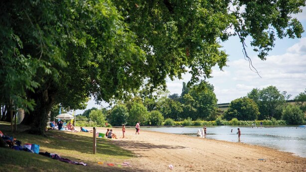 A lakeside beach with people relaxing and playing.