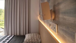 A hotel room with a bed, a wall-mounted light fixture, and a window with curtains.