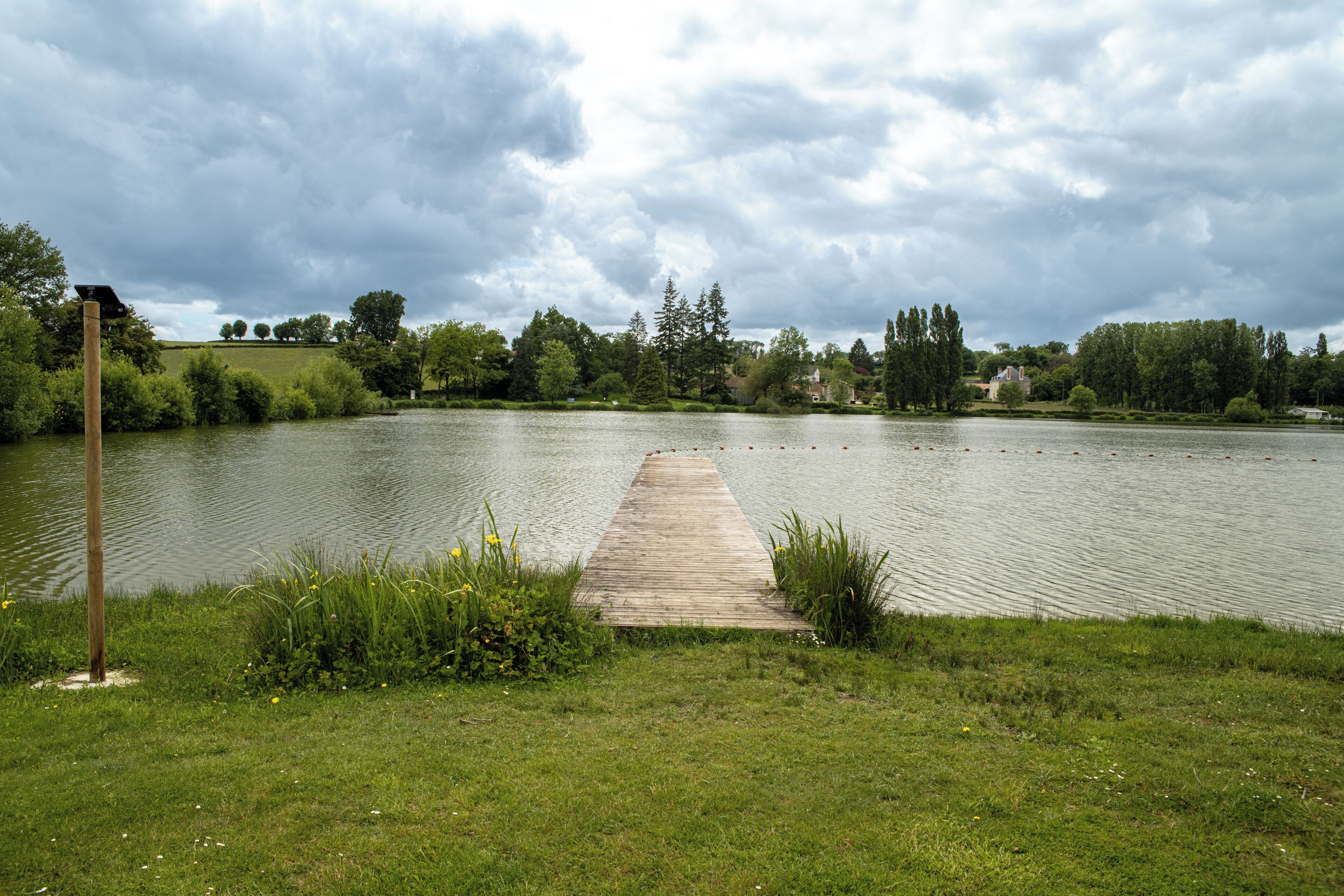 A wooden dock extending into a calm lake surrounded by lush greenery and trees.