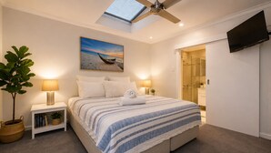 A bedroom with a bed, bedside lamps, a ceiling fan, a TV, a painting, and a plant. - Sea Renity On Earnshaw (West Busselton)