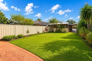 A residential backyard with a well-maintained lawn, a brick patio, and a white fence. - Sea Renity On Earnshaw (West Busselton)