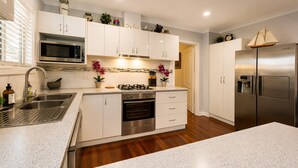 A modern kitchen with stainless steel appliances, white cabinetry, and a central island. - Sea Renity On Earnshaw (West Busselton)