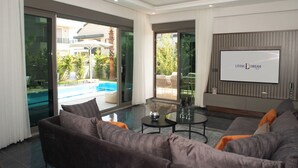 A modern living room with a large sofa, a coffee table, and a TV screen displaying "Living Dream." - Living Dream Villa Harmony (Antalya)