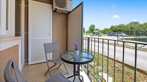 A balcony with a table and chairs, a sliding door, and a view of the street. - Apartment White (Rovinj)