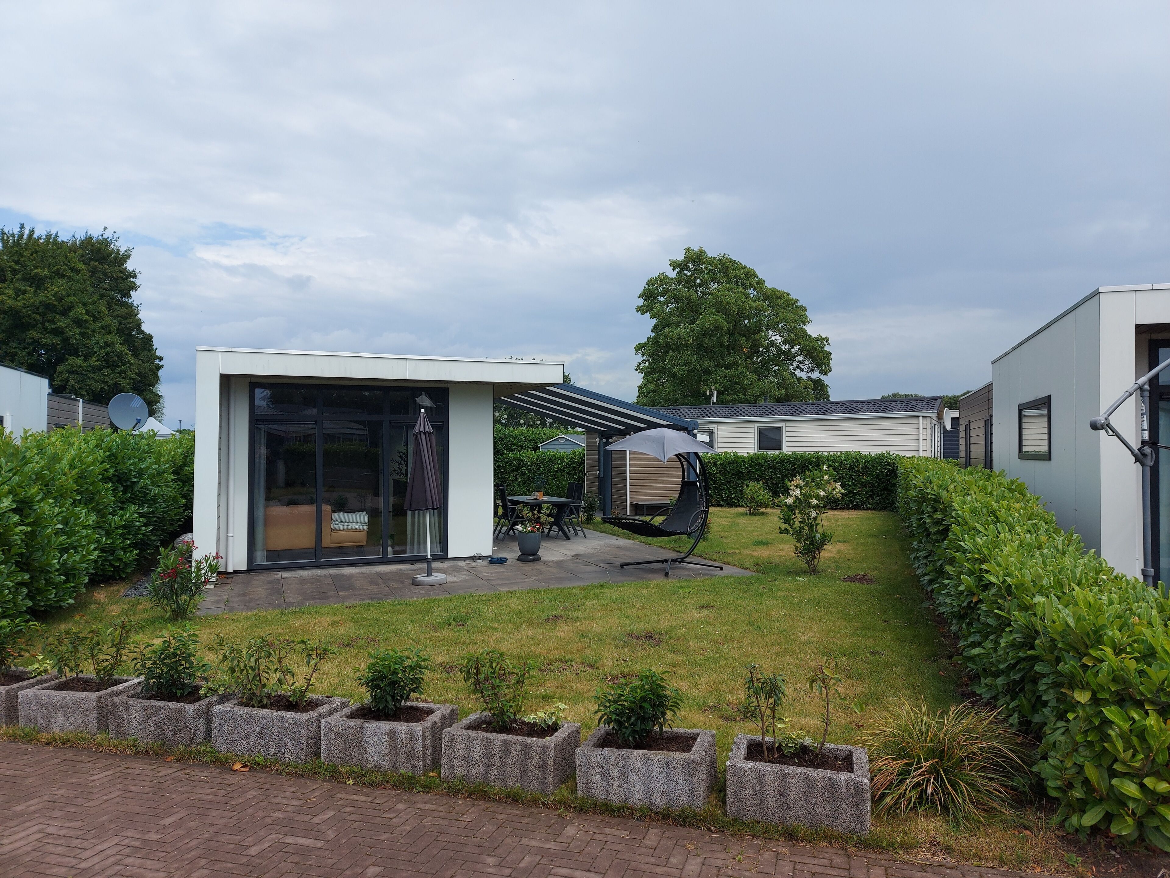 A modern outdoor patio area with a seating arrangement, a small garden with planters, and a building with large windows and a covered seating area.