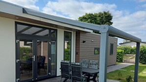 A modern house with a patio area featuring a table and chairs, a covered seating area, and a glass door entrance.