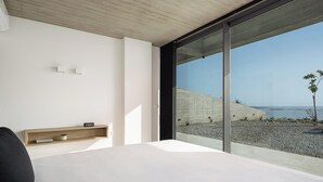 Een moderne slaapkamer met een groot bed, een houten plank en uitzicht op het strand.