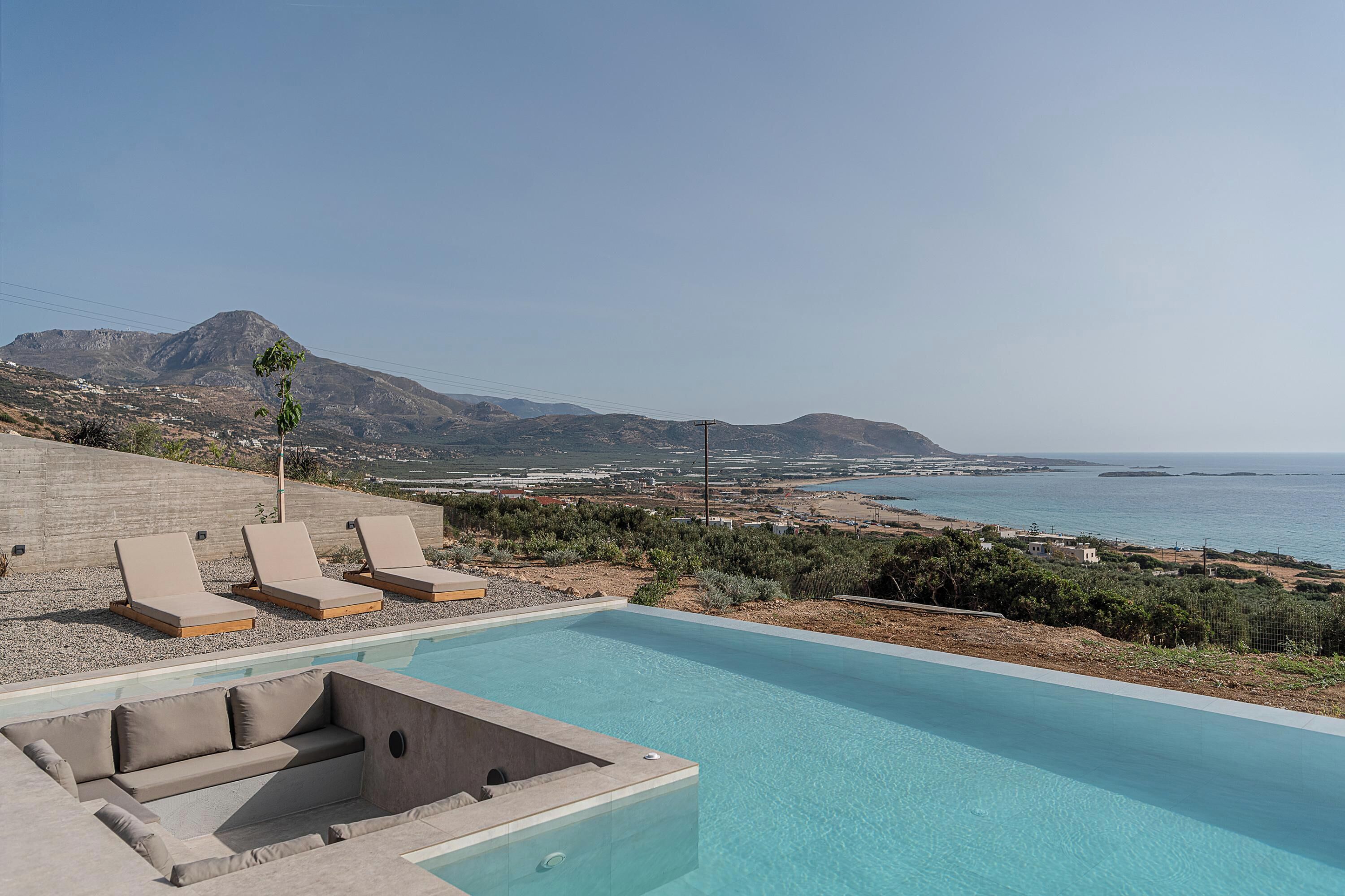 Zona de piscina con sillones de descanso y bañera de hidromasaje, con vistas a un paisaje costero con montañas y el mar.