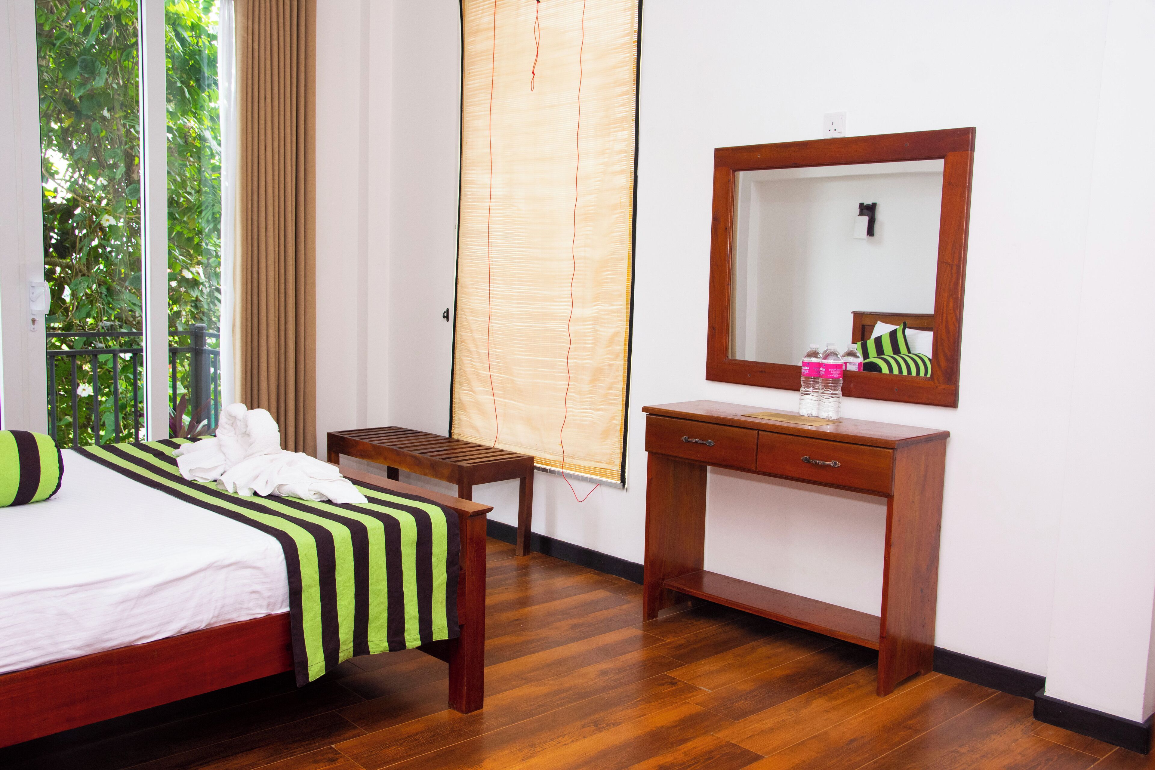 A hotel room with a bed, a wooden desk, a mirror, and a window with curtains.