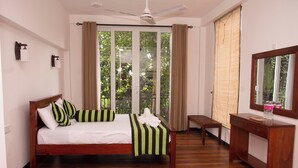 A bedroom with a wooden bed, a bedside table, a mirror, and a view through a large window with curtains. - Peaceful Peak (Kandy)