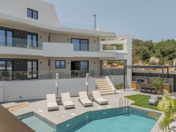 A modern two-story building with a rooftop pool, outdoor seating, and a barbecue area.