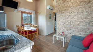 A kitchen with granite countertops, a dining area with a wooden table and chairs, a stone wall, and a gray sofa with red cushions.