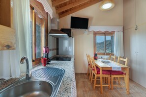A kitchen with a stainless steel sink, wooden dining table, chairs, and a television mounted above the counter.
