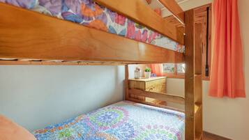 Een stapelbed met een kleurrijke quilt, een houten hoofdbord en een raam met gordijnen.