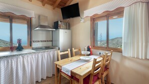 A kitchen with a dining table, chairs, a TV mounted on the wall, and a view through the window.
