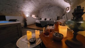 Tunnelmallinen huone, jossa on maalaishenkinen kivikatto, sinisellä peitolla varustettu sänky, yöpöytä, jossa on kynttilöitä, laseja ja pullo.