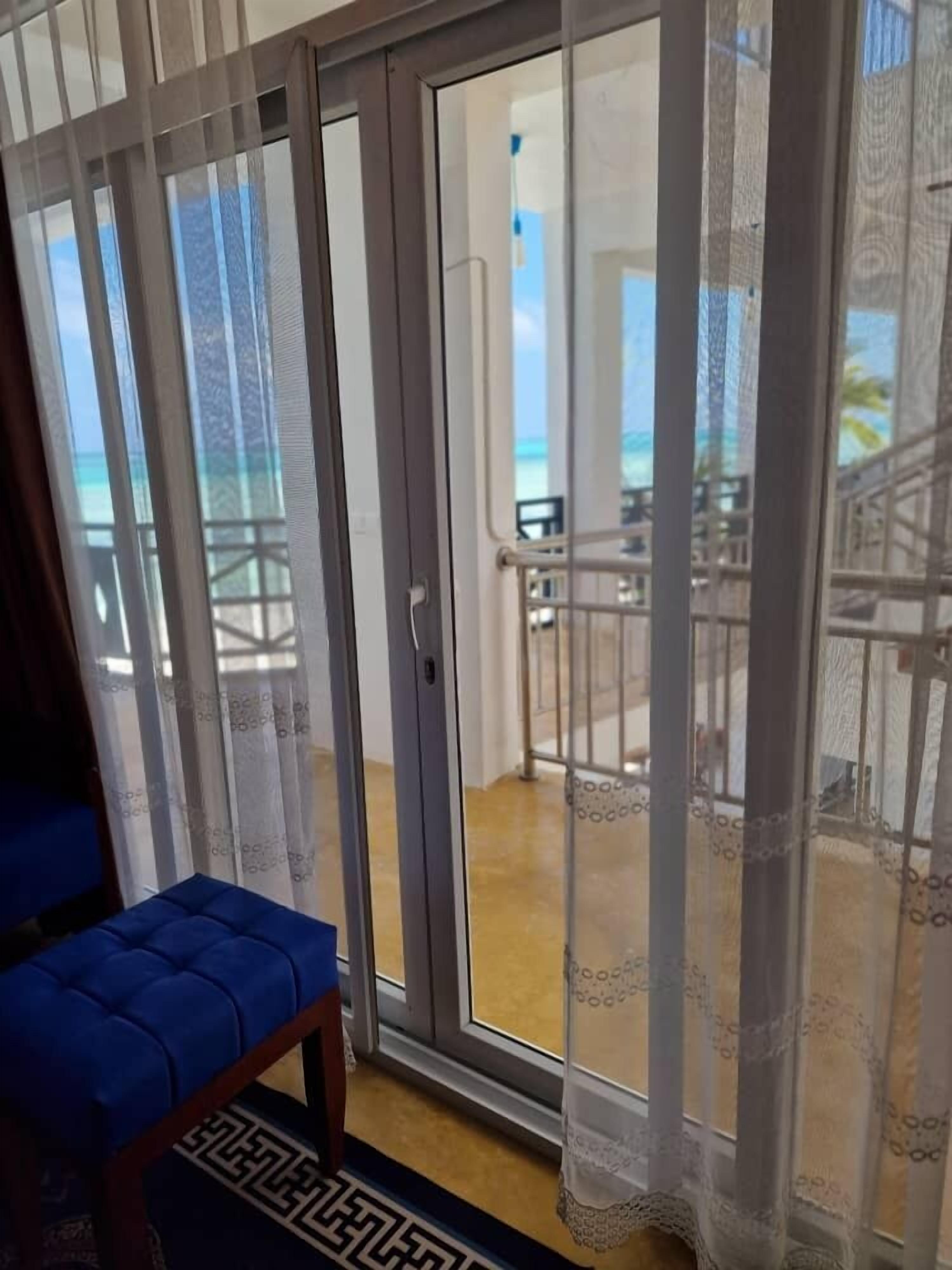 A room with a sliding glass door leading to a balcony with a view of the ocean.