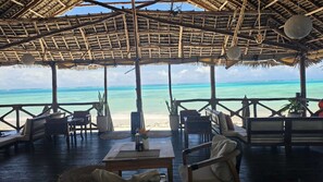 An outdoor seating area with a view of the ocean, wooden furniture, and a thatched roof structure. - Mia Boutique Hotel (Michamvi)
