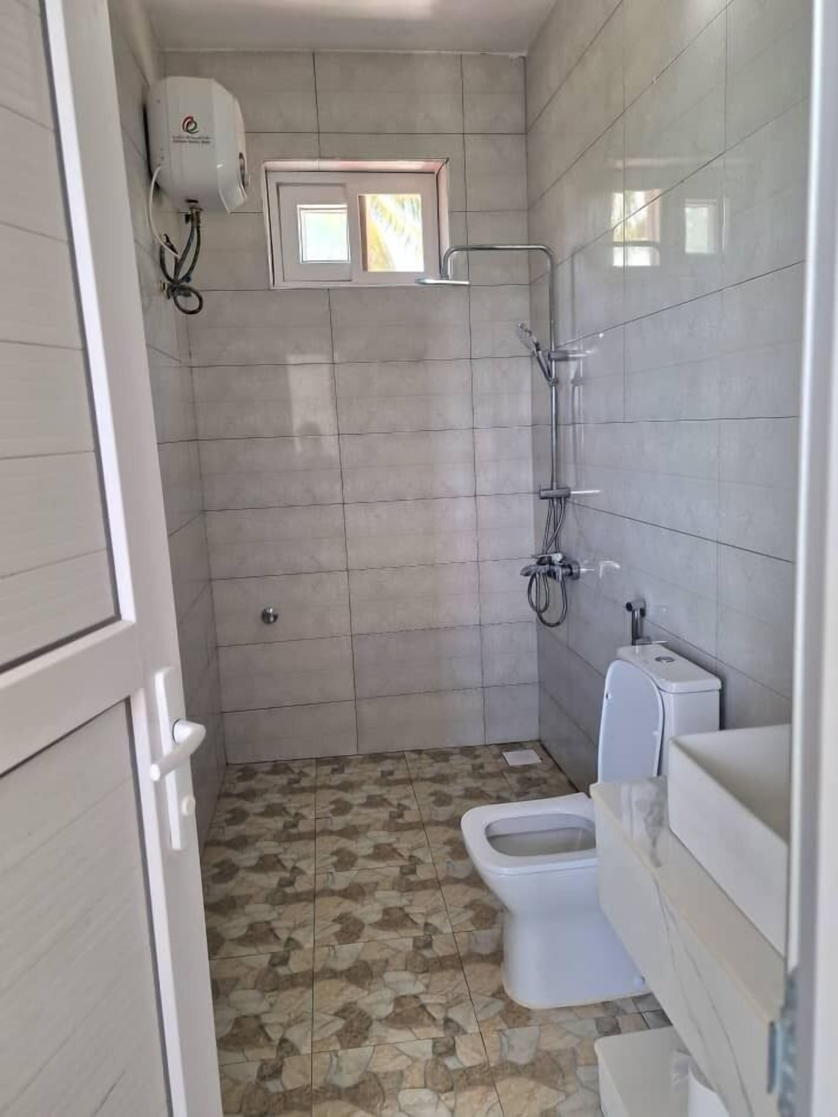 A bathroom with a shower, toilet, and a small window.