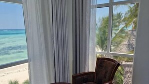 A room with a large window overlooking a beach. There is a round table with two chairs. - Mia Boutique Hotel (Michamvi)