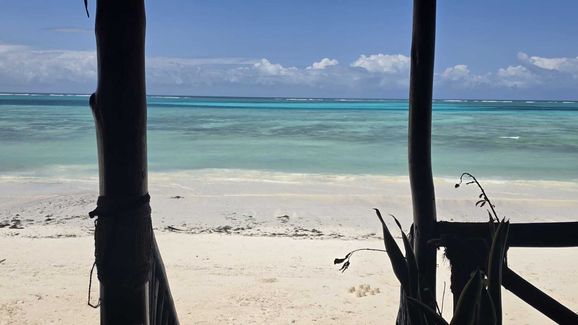 Vista de una playa con agua turquesa cristalina, orilla de arena y construcciones de madera.