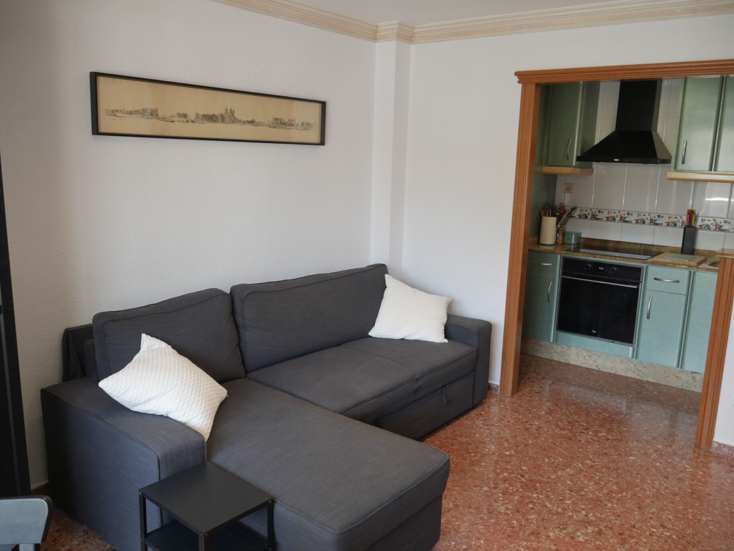 A living room with a grey sofa, a small black side table, and a framed cityscape picture on the wall.
