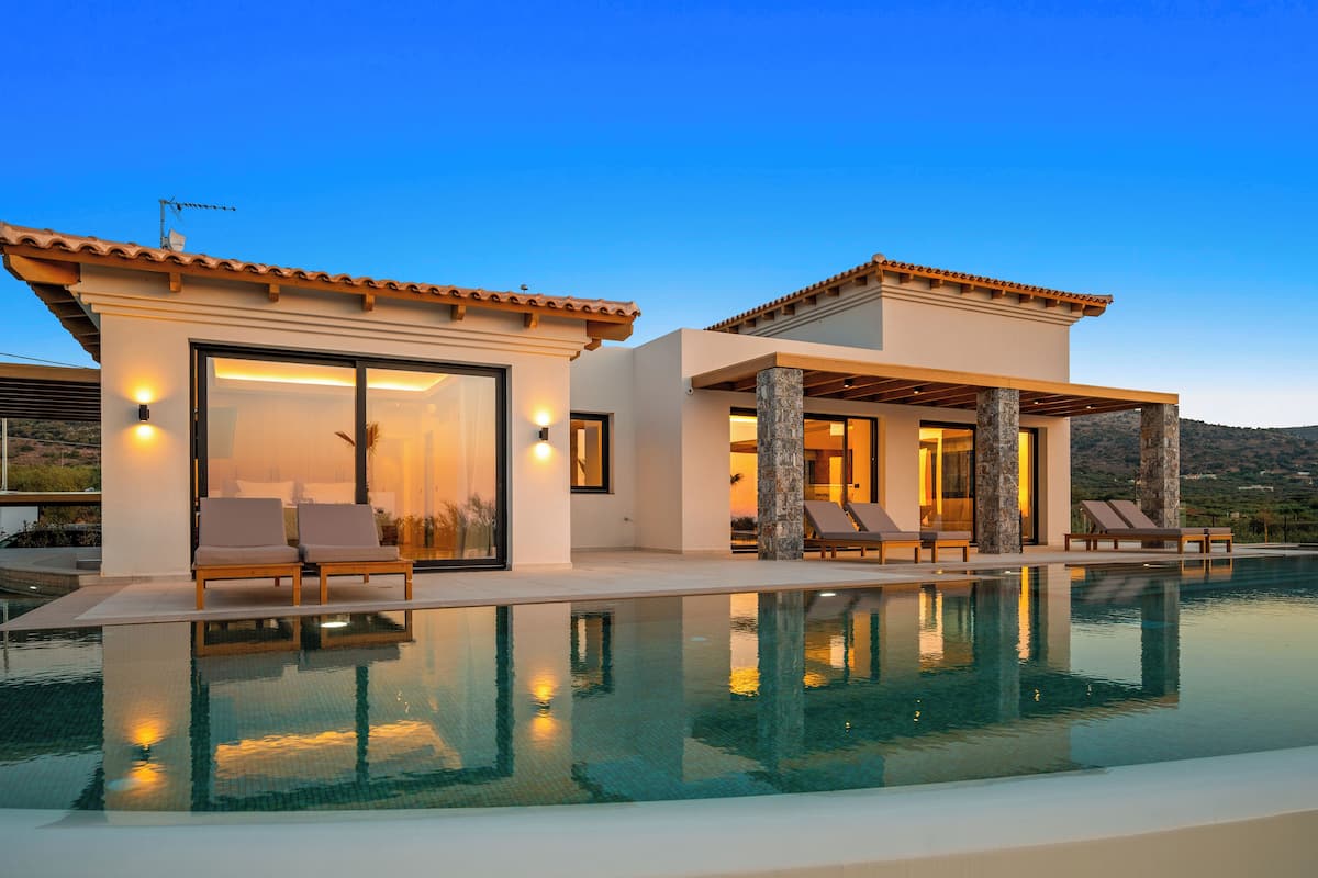 Una villa moderna con piscina infinita, ventanas amplias y zona de estar exterior.