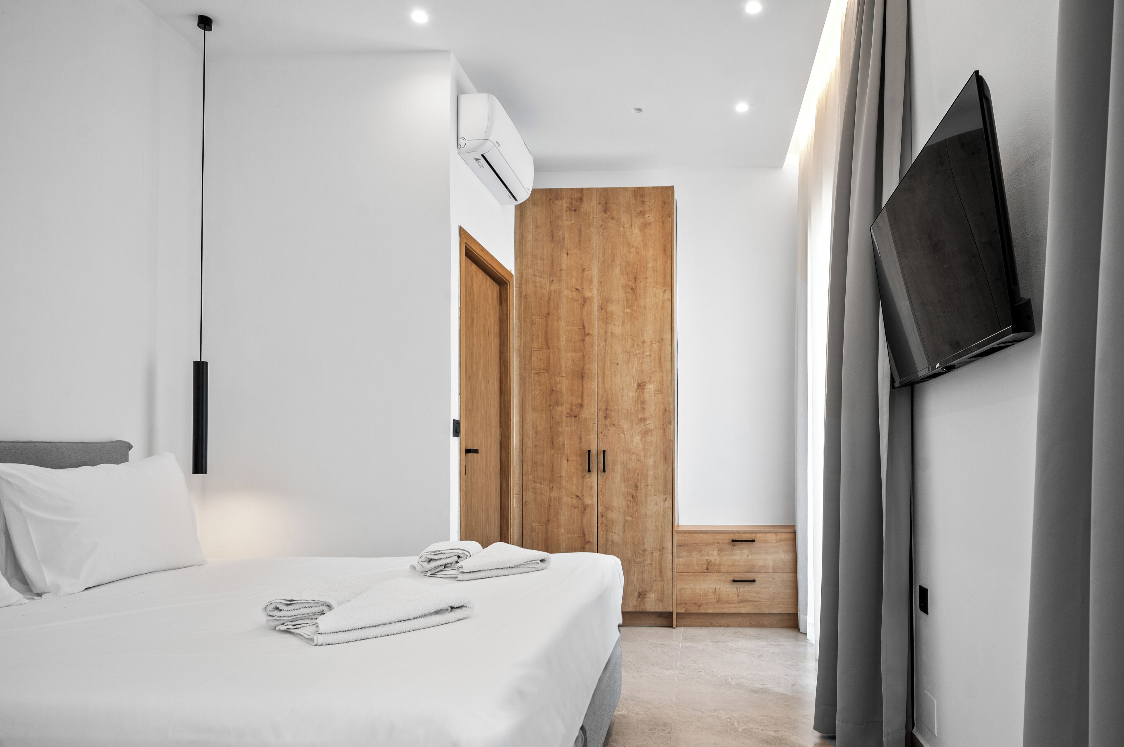Une chambre d’hôtel moderne équipée d’un lit, d’une armoire en bois, d’un téléviseur à écran plat fixé au mur et d’un appareil de climatisation installé au plafond.