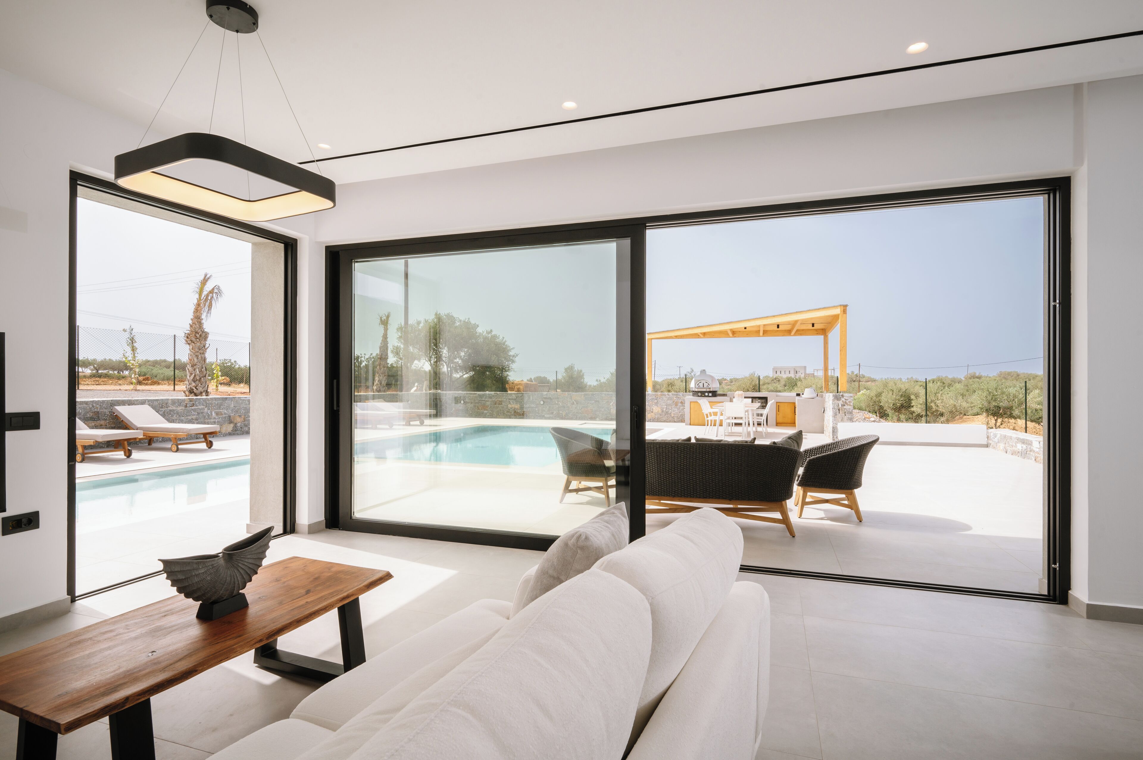 A modern living room with a large glass door leading to a pool area, a wooden table, and a sofa.