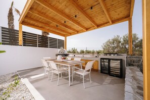 An outdoor patio with a wooden pergola, a grill, and a stone wall.