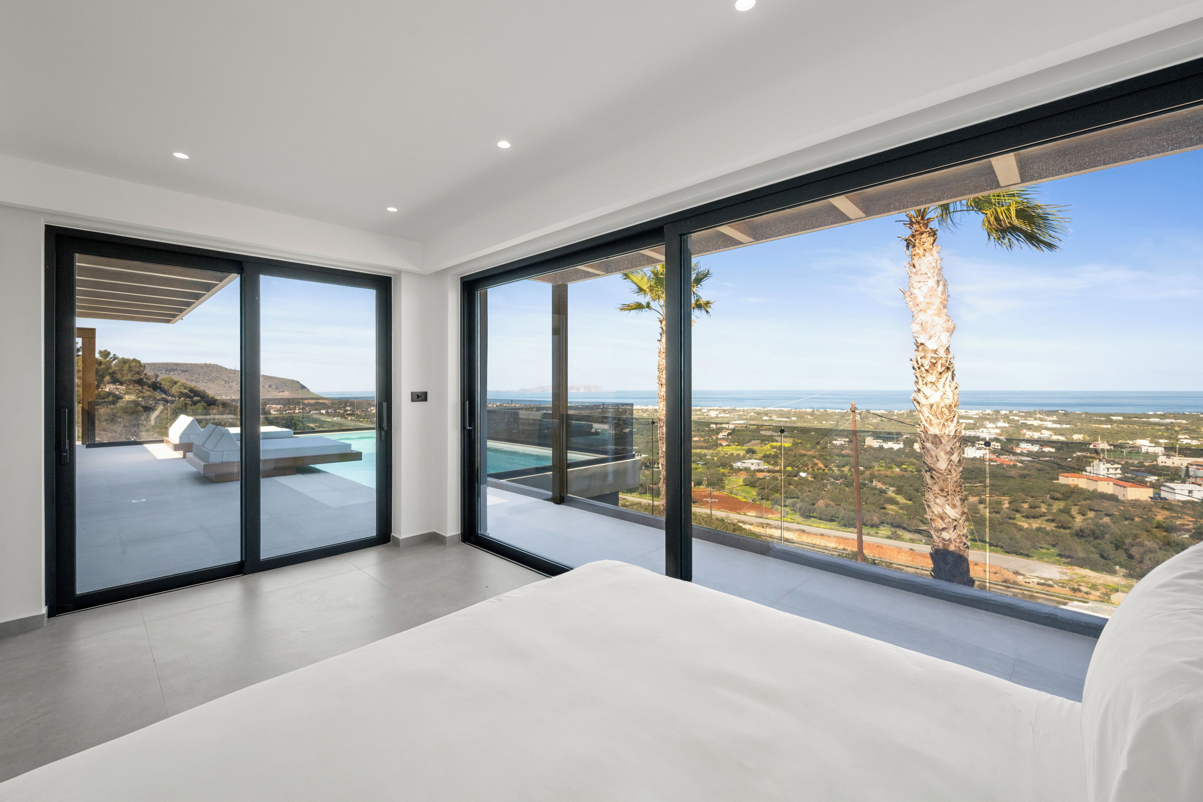 A modern bedroom with large sliding glass doors leading to a balcony with a pool and a view of the landscape.