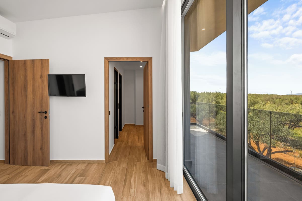Una habitación de hotel moderna con suelo de madera, un ventanal con vistas al exterior y un televisor de pantalla plana montado en la pared.
