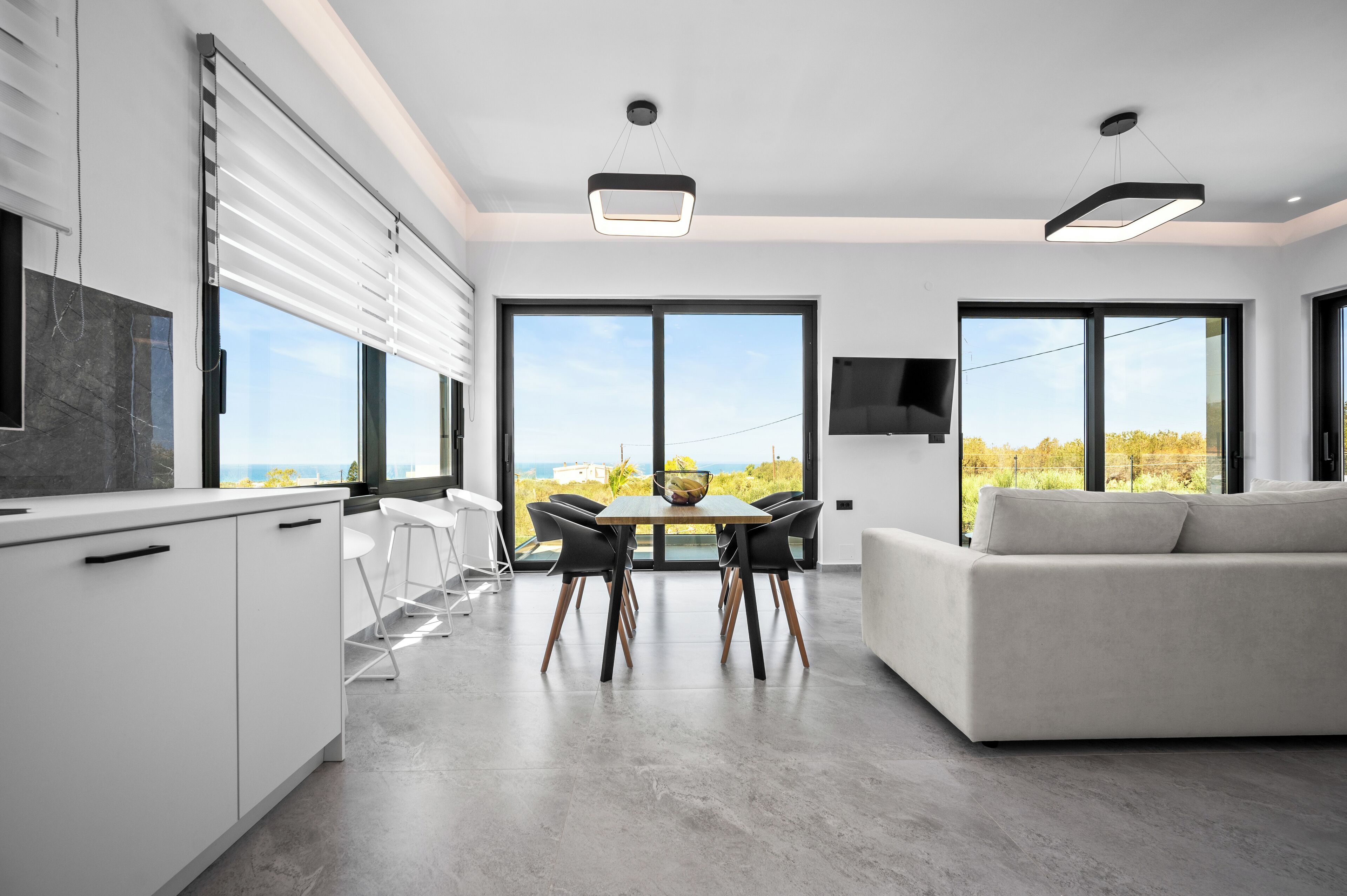 A modern kitchen with white cabinets, a dining table with chairs, and a large window offering a view of the outdoors.