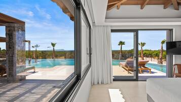 A modern hotel room with a large window, a bed, and a view of a pool and palm trees.