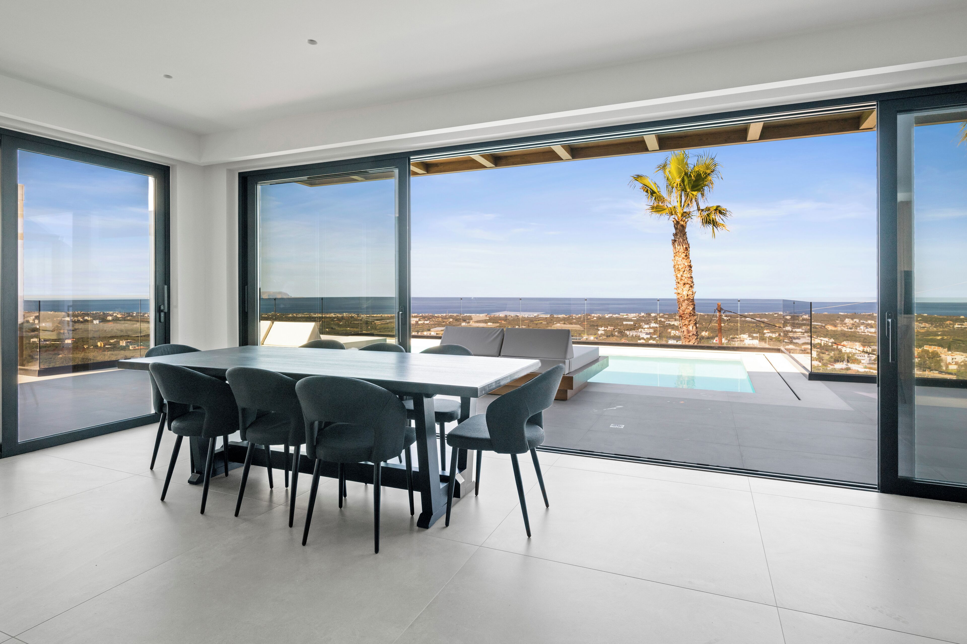 Un comedor moderno con mesa y sillas, piscina y vistas al océano y una palmera.