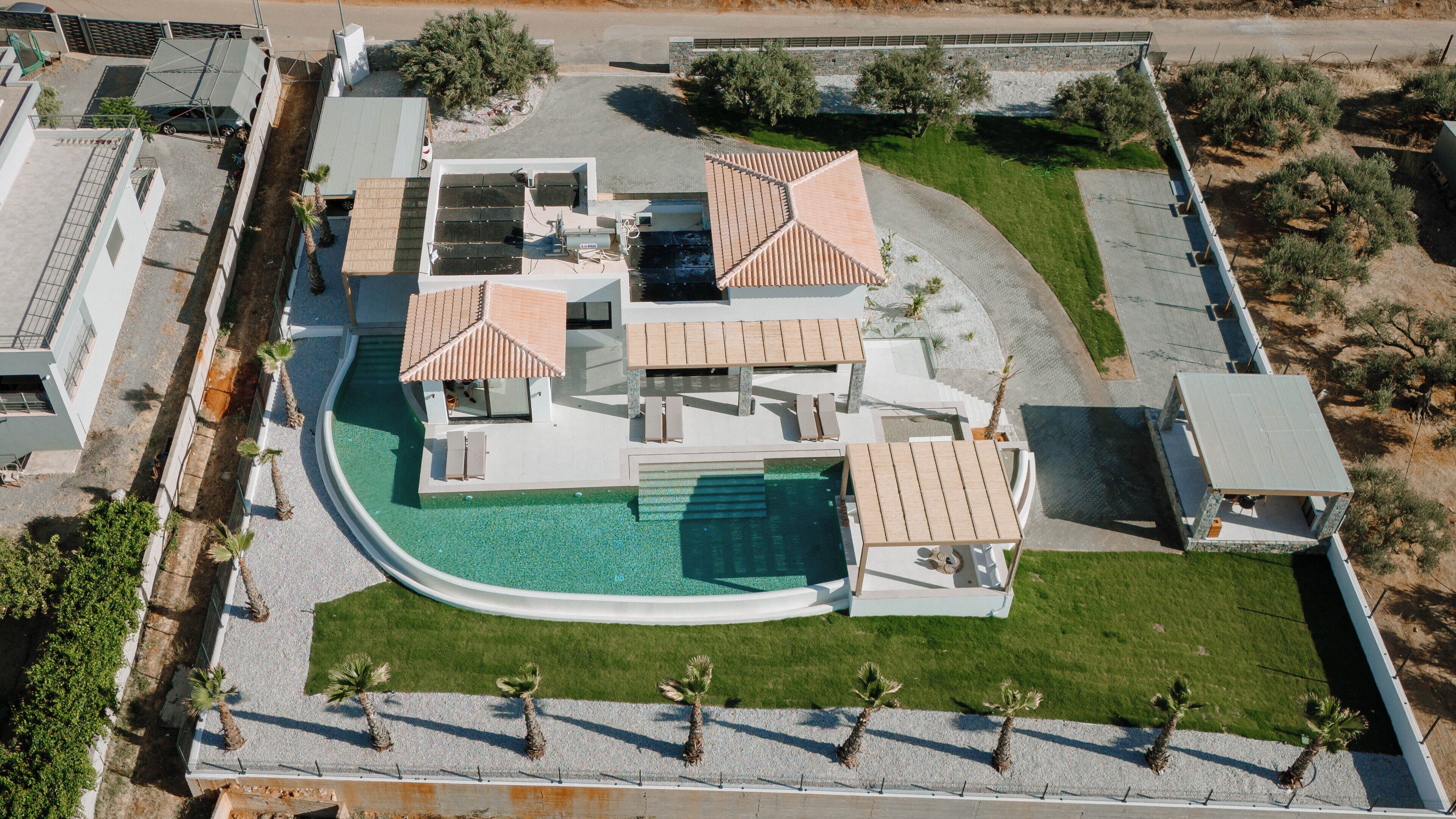 An aerial view of a modern house with a swimming pool, multiple outdoor seating areas, and a well-maintained lawn.