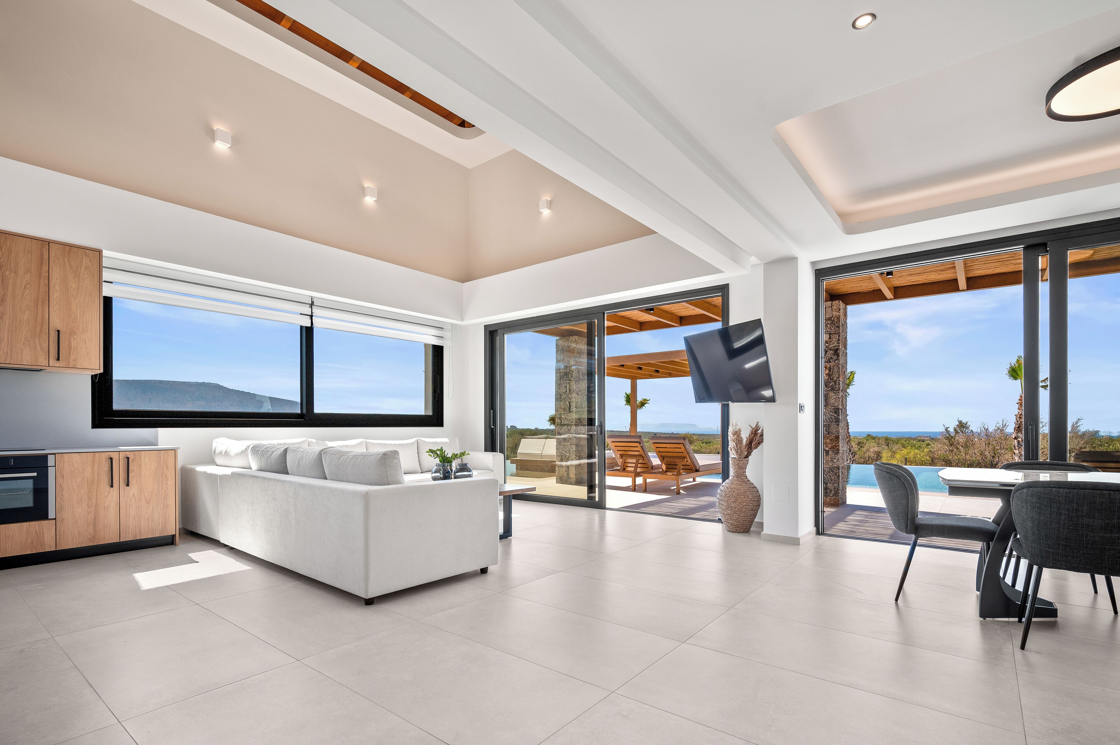 Un salon moderne avec un canapé blanc, un coin repas comprenant une table et des chaises, et de grandes fenêtres offrant une vue sur l’océan.