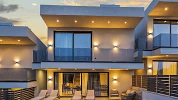 A modern two-story house with a balcony, outdoor seating, and a large window.