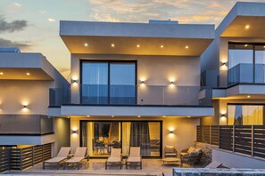 A modern two-story house with a balcony, outdoor seating, and a large window.