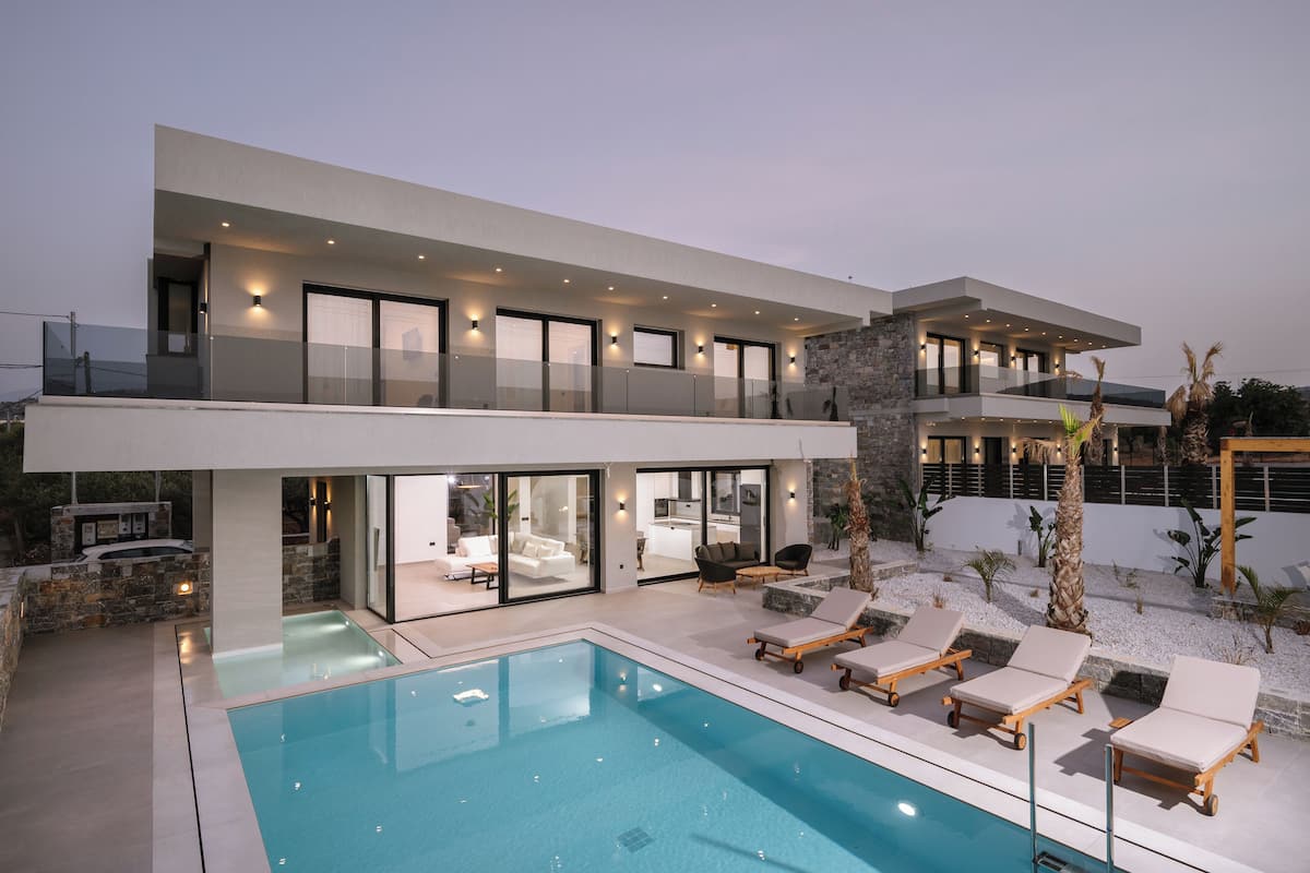 Una casa moderna de dos pisos con piscina, mobiliario exterior y fachada de piedra.