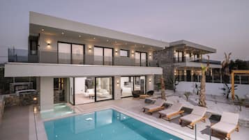 A modern two-story house with a swimming pool, outdoor seating, and a stone facade.