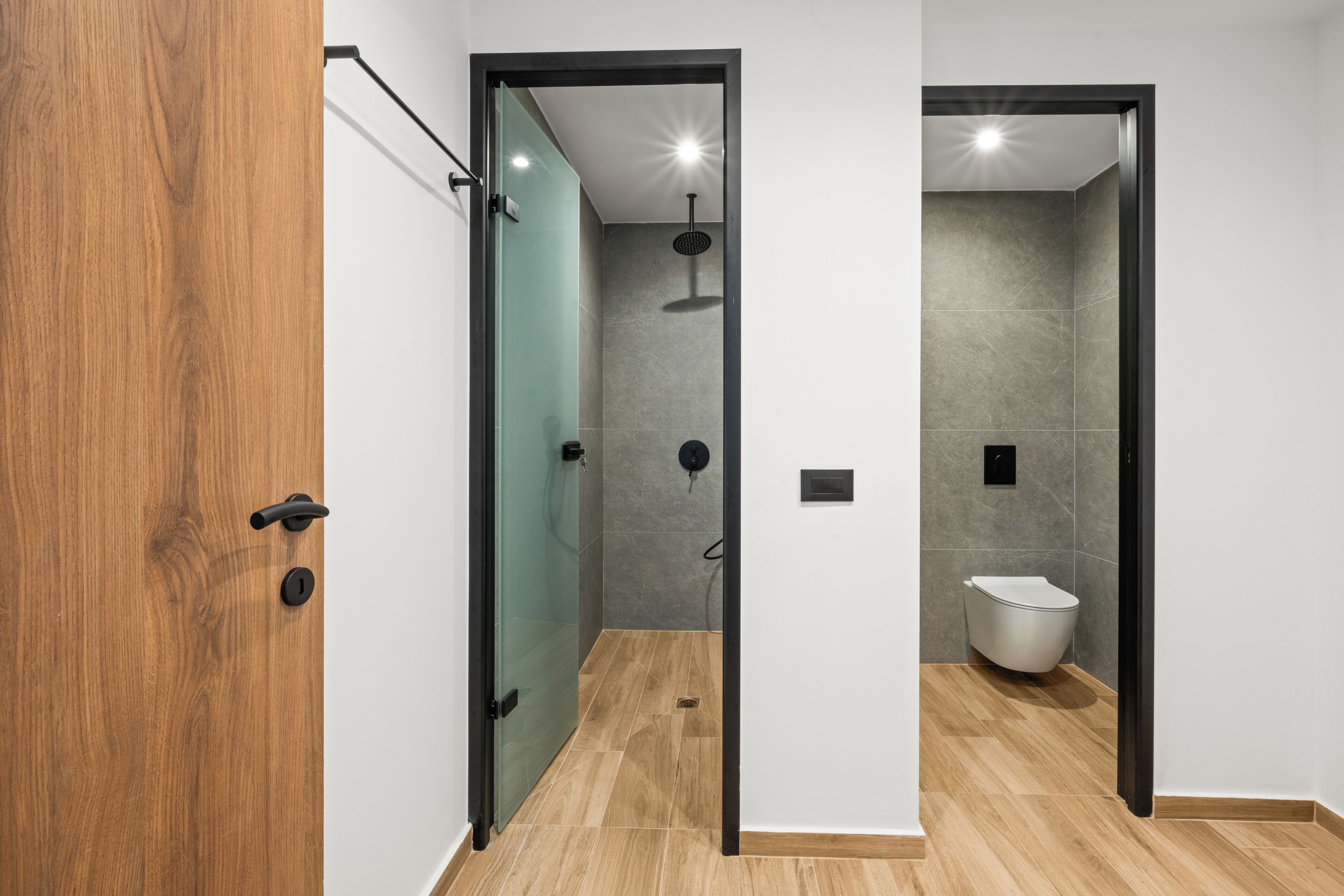 A modern bathroom with a glass shower enclosure, a toilet, and a wooden floor.