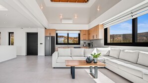 A modern kitchen with wooden cabinets, a large window, and a view of the outdoors. - Temma Villas (Hersonissos)