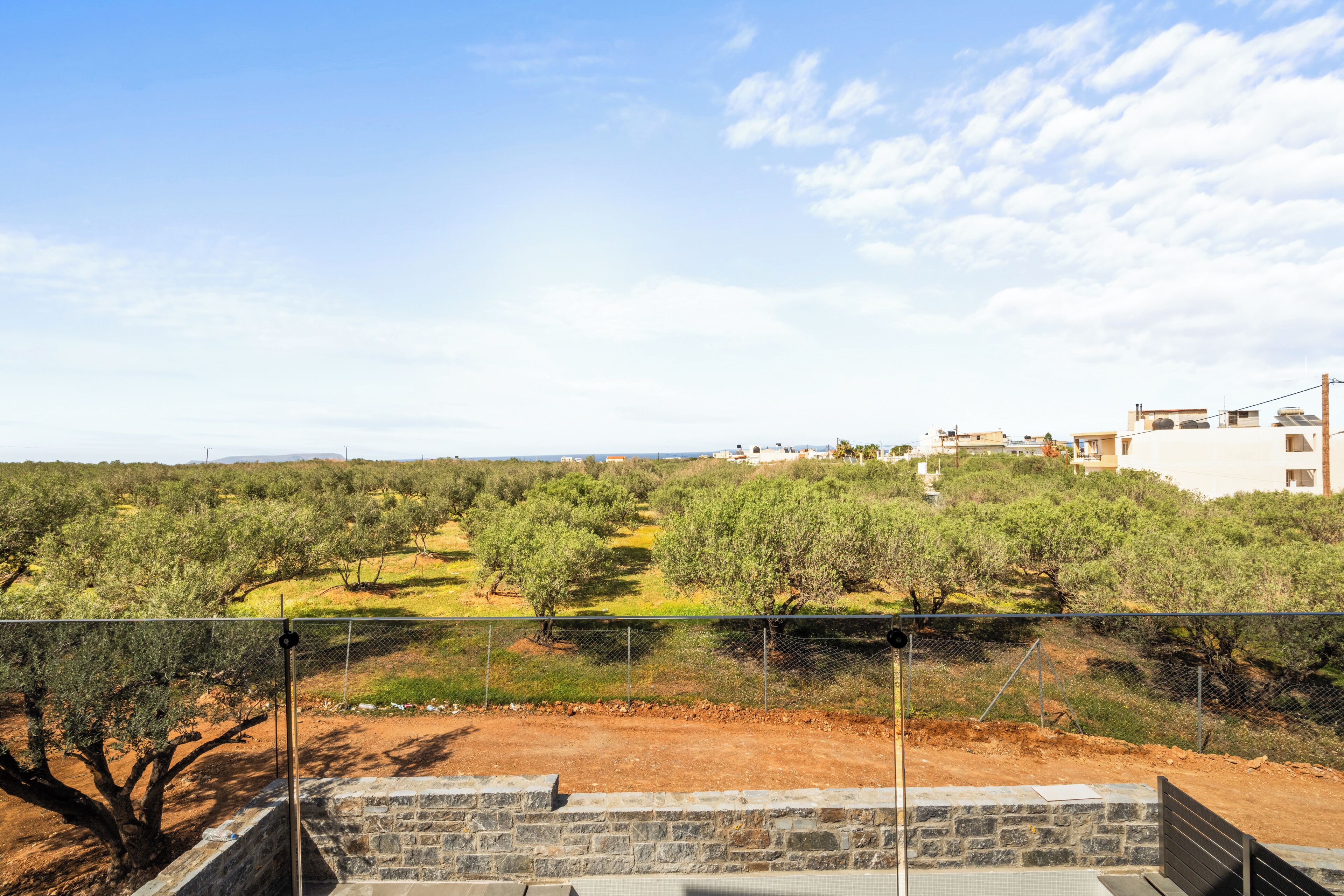 A view from a balcony overlooking a landscaped area with olive trees and a distant building complex.