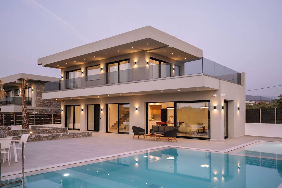 Una casa moderna de dos pisos con piscina, ventanas amplias y mobiliario exterior.