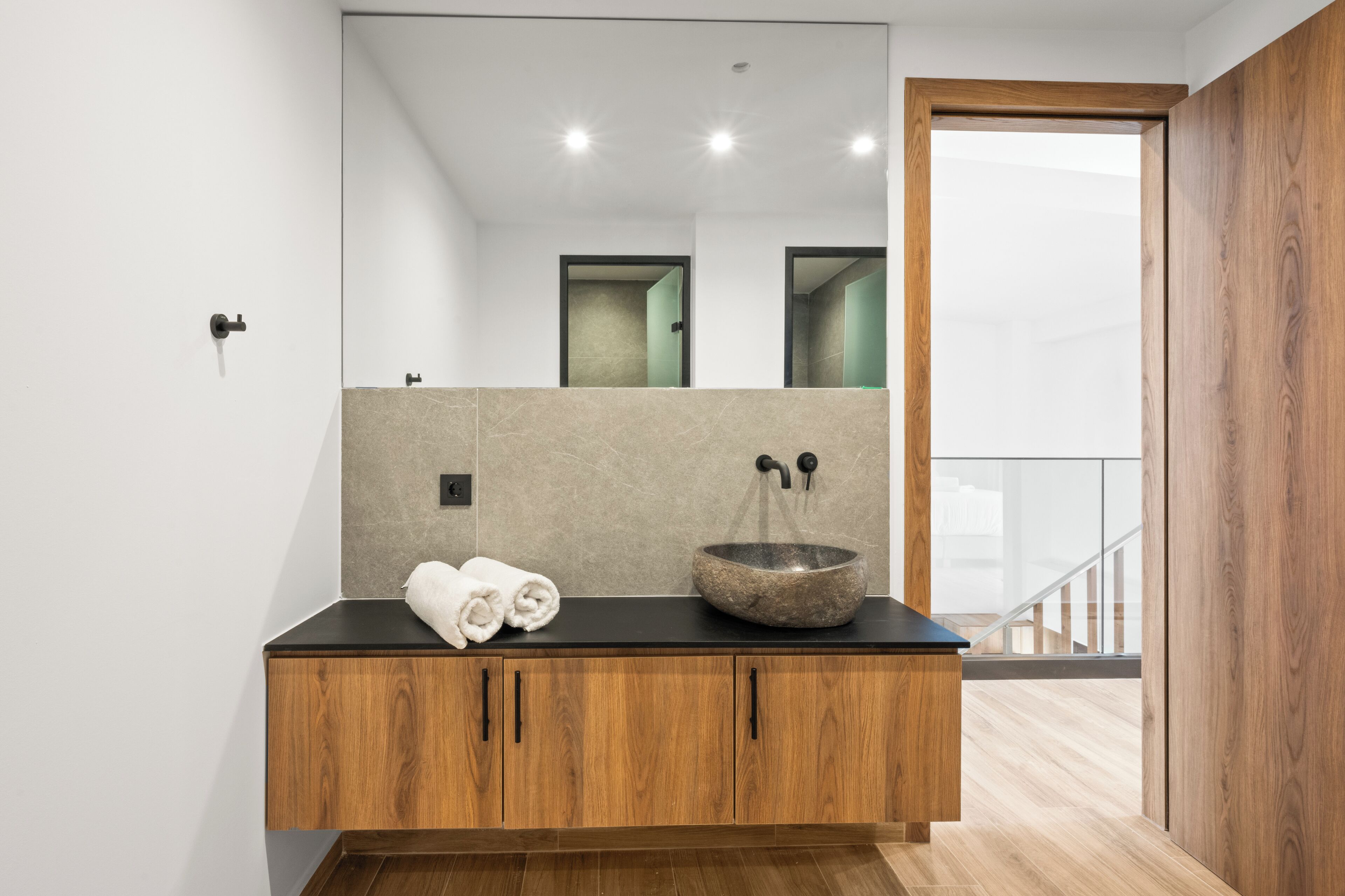 Un baño moderno con tocador de madera, lavamanos de piedra y un espejo grande.