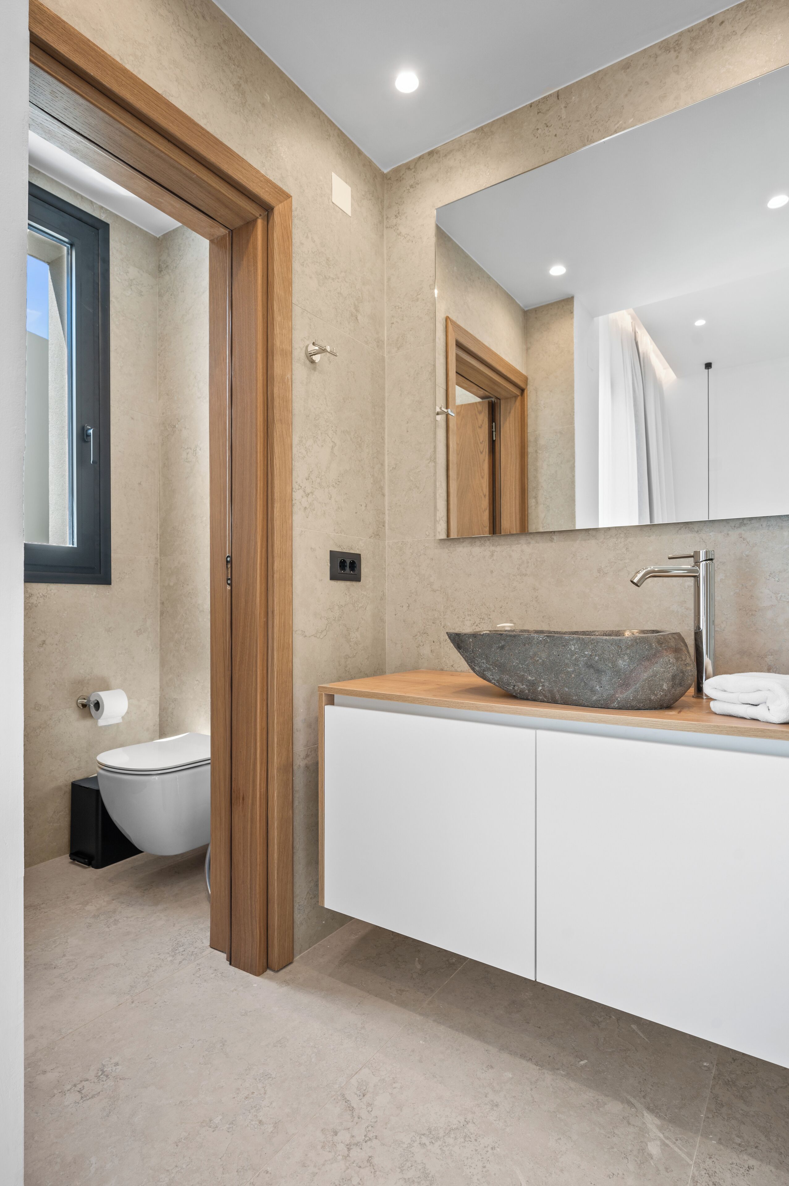 A modern bathroom with a stone sink, wooden door, and a large mirror.