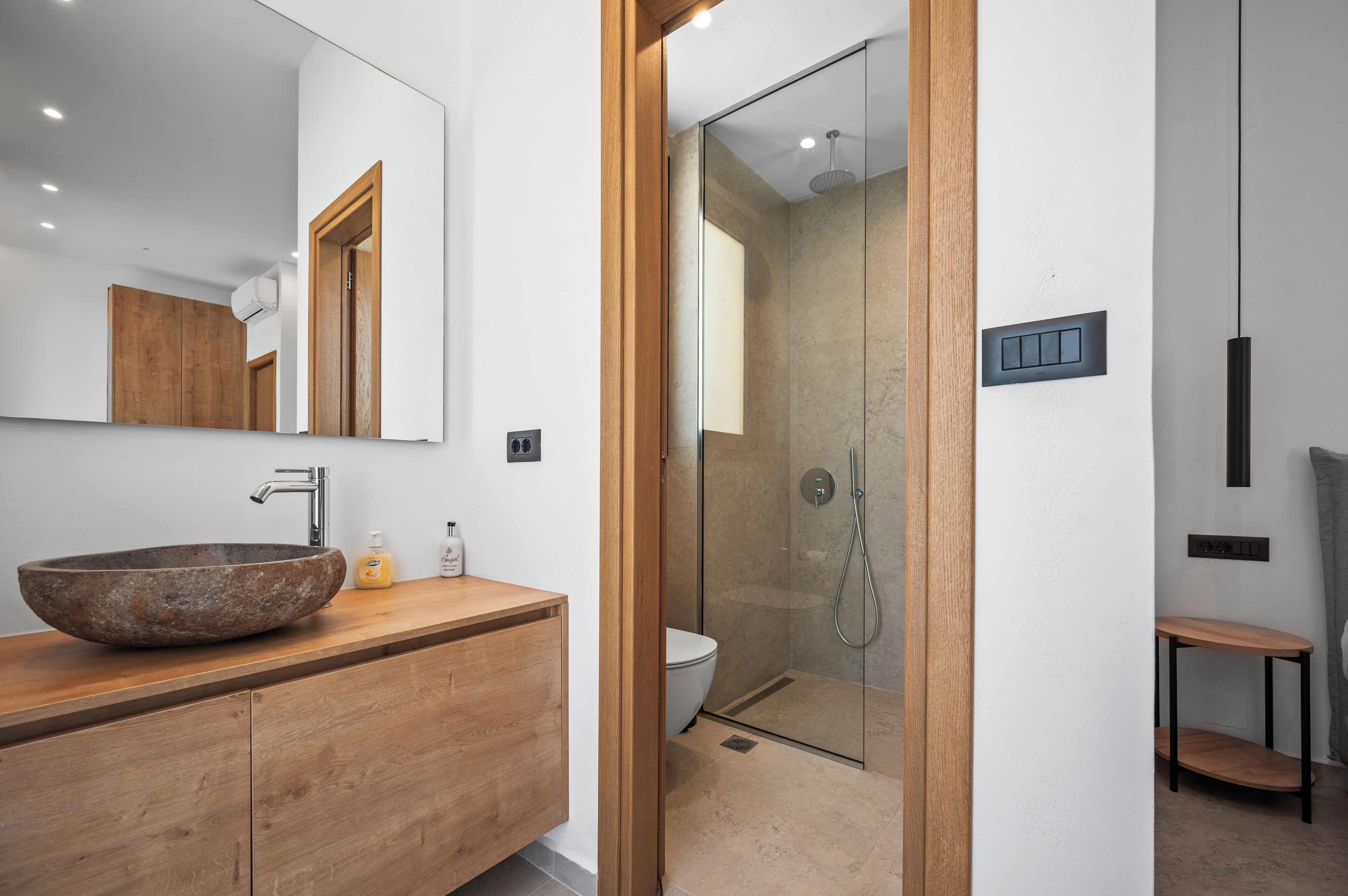A modern bathroom with a large stone sink, wooden vanity, a glass-enclosed shower, and a minimalist design.