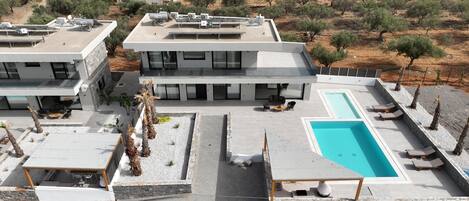 Un edificio moderno con piscina en la azotea, mobiliario de exterior y paneles solares.