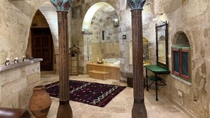 A historic interior with stone walls, a wooden bench, a large mirror, and a patterned rug. - 1860 KADIEVİ (Ürgüp)